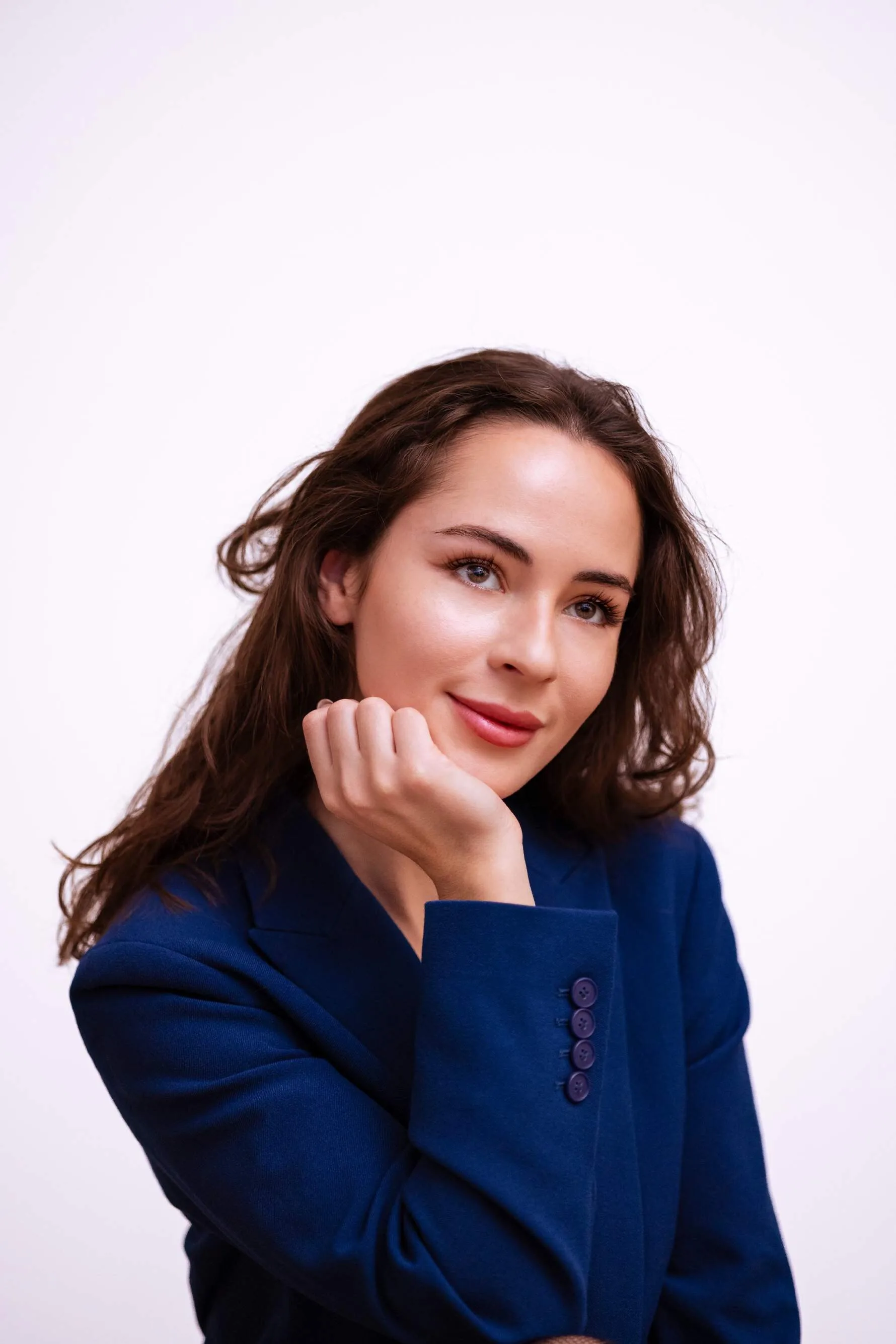 Studio portrait of a woman with dark wavy hair in a blue blazer, resting her chin on her hand