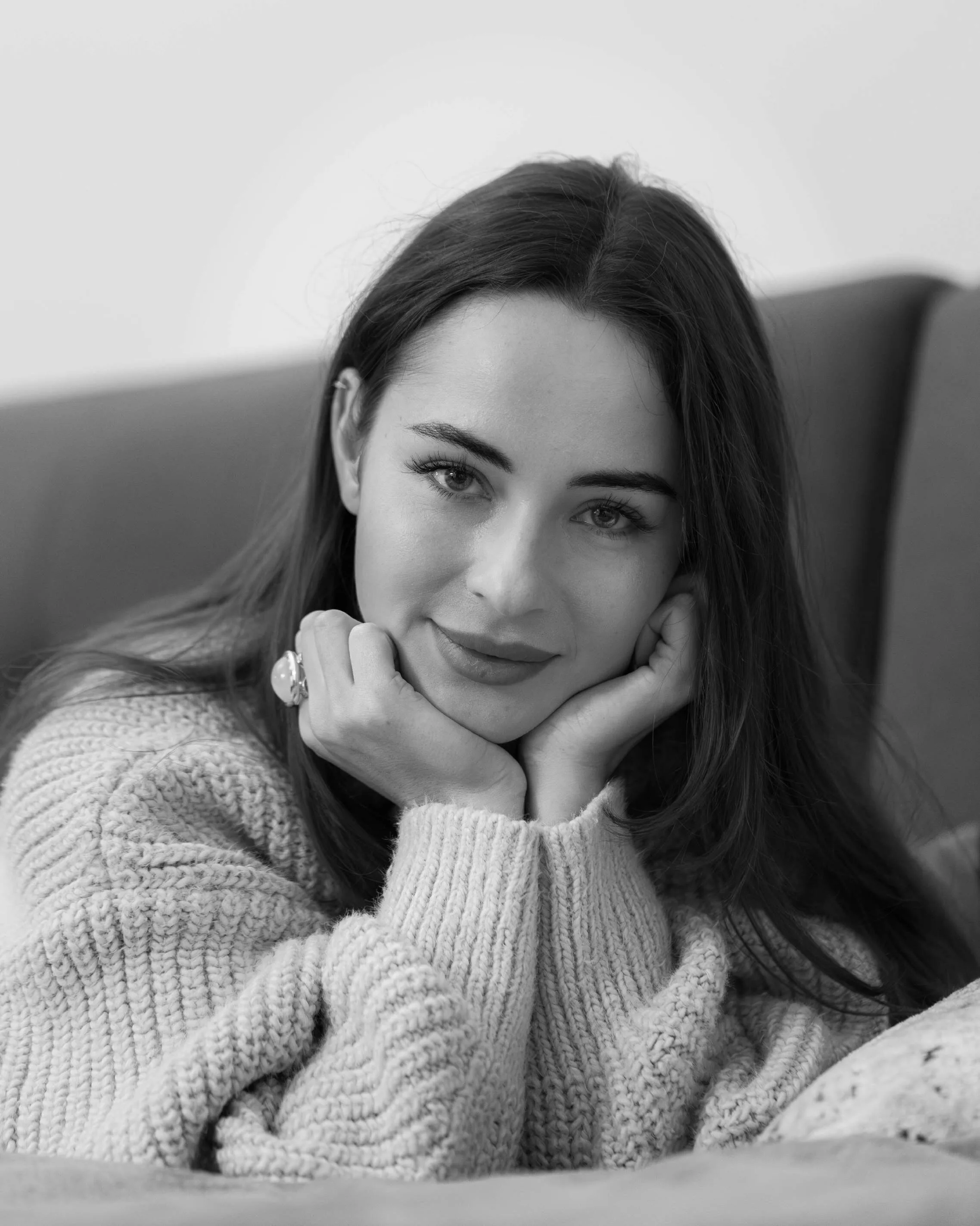 Black and white portrait of a woman in a knitted sweater, resting her face on her hands