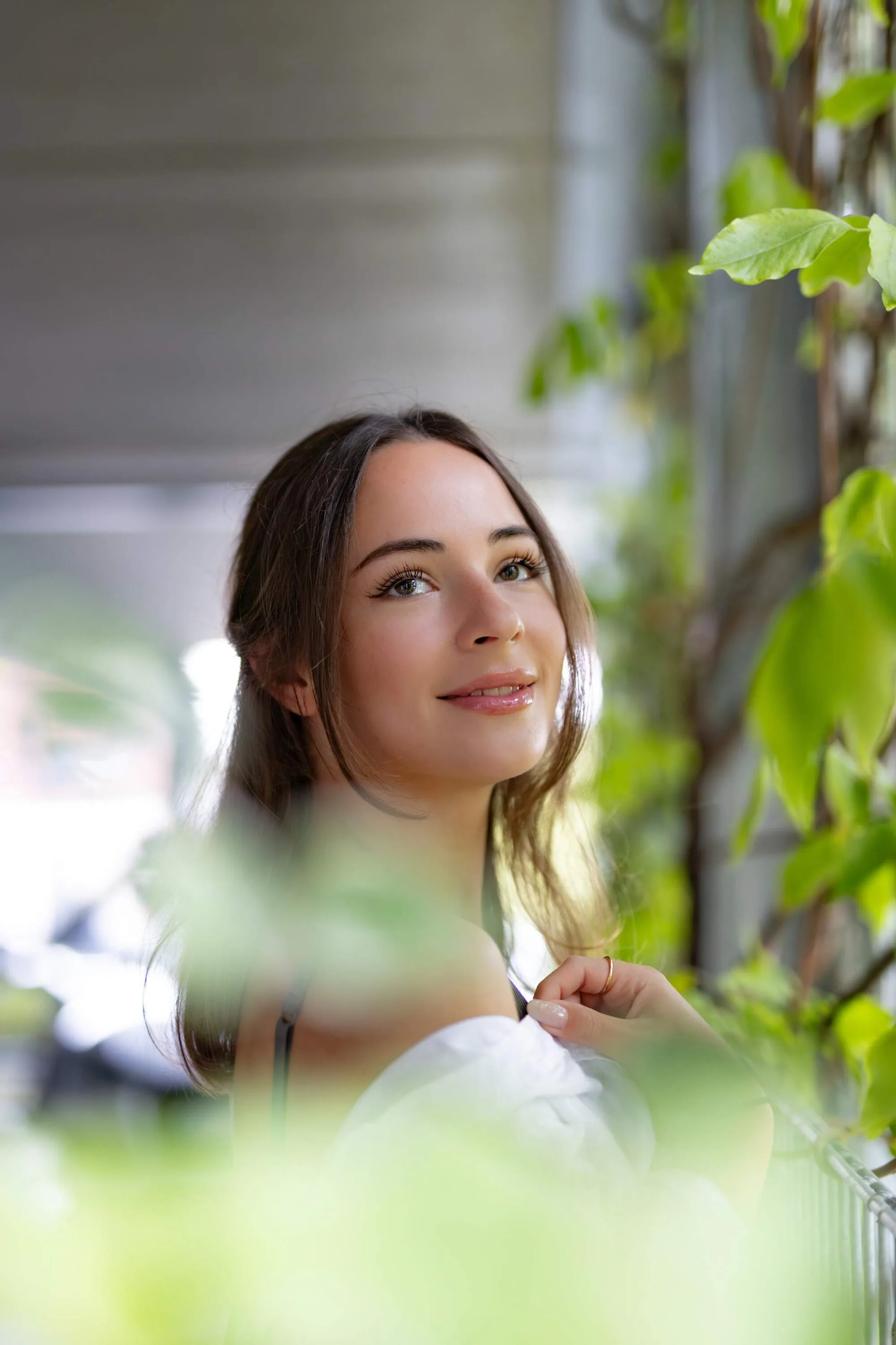 Portrait of a woman looking over her shoulder, framed by blurred green leaves